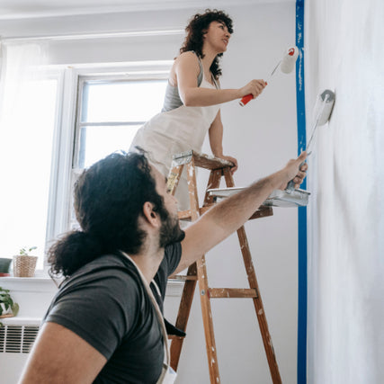 PaintsA couple painting an interior room wall together with paint rollers.