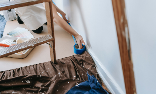A close-up of paint tape being applied to the bottom of a wall.
