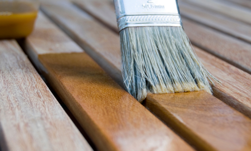 A close up of a paint brush applying wood stain to wood boards.