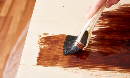 A close up of wood stain being applied by wood with a brush.