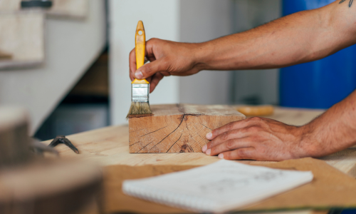 Wood stain being applied to a wood block with a brush.